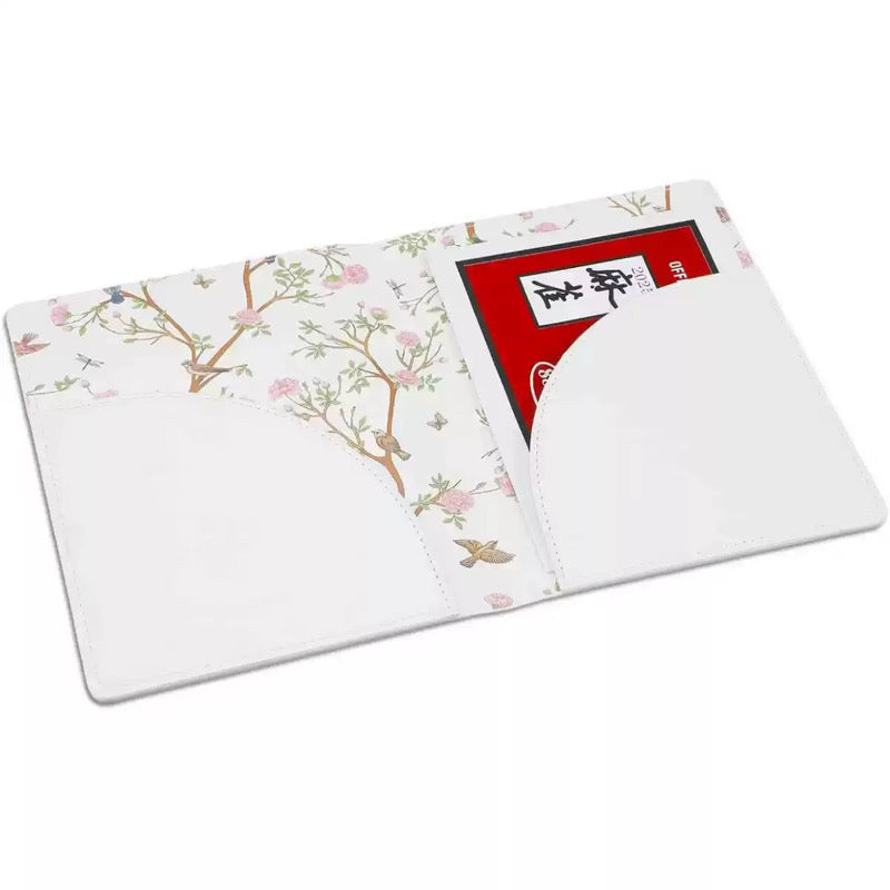A white leather passport cover with a delicate pink and green floral branch pattern on the cover, shown open with card slots containing a red and black card.
