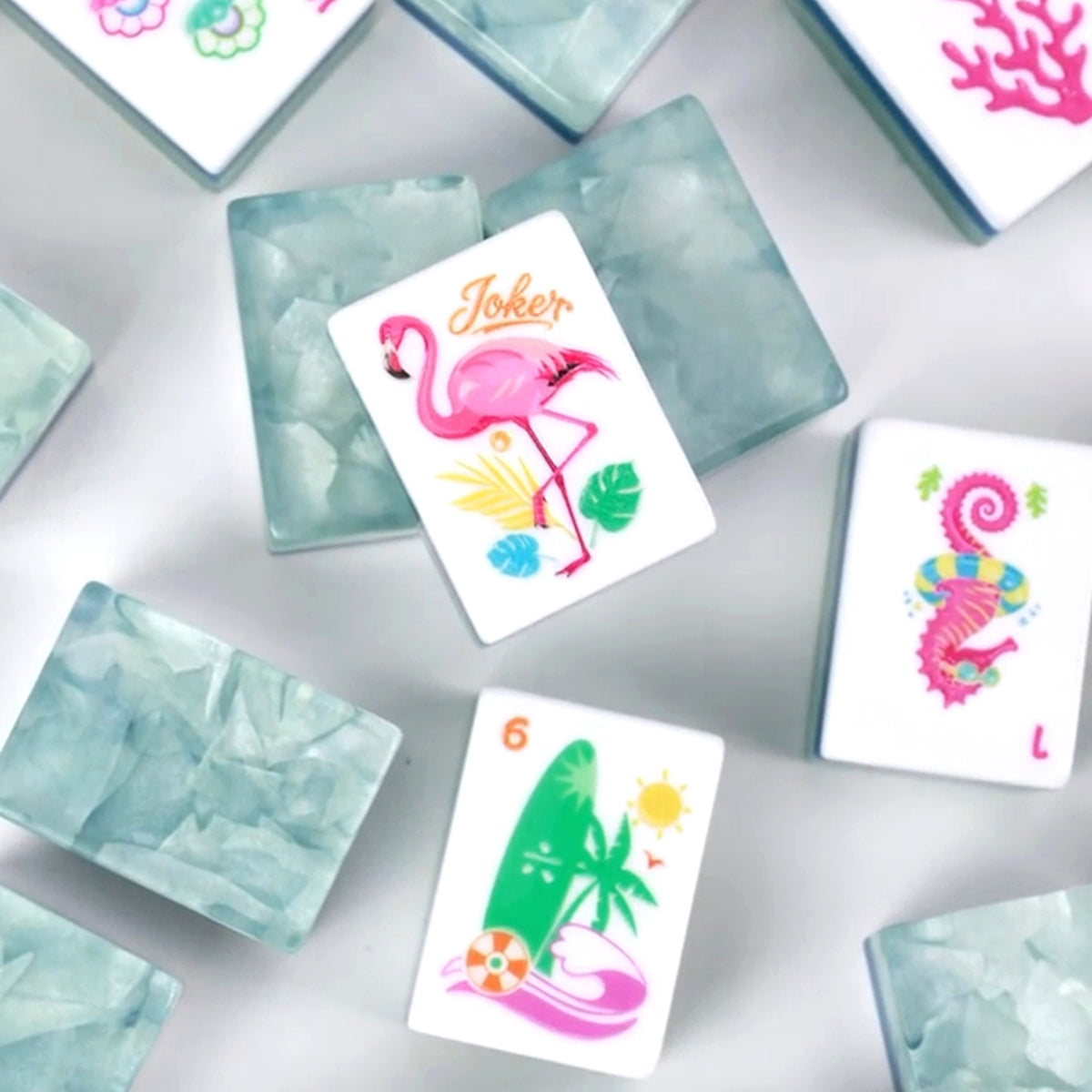 Colorful American Mahjong tiles with flamingos, florals, coral-inspired Bams, decorative Winds and translucent blue-green tile backs.