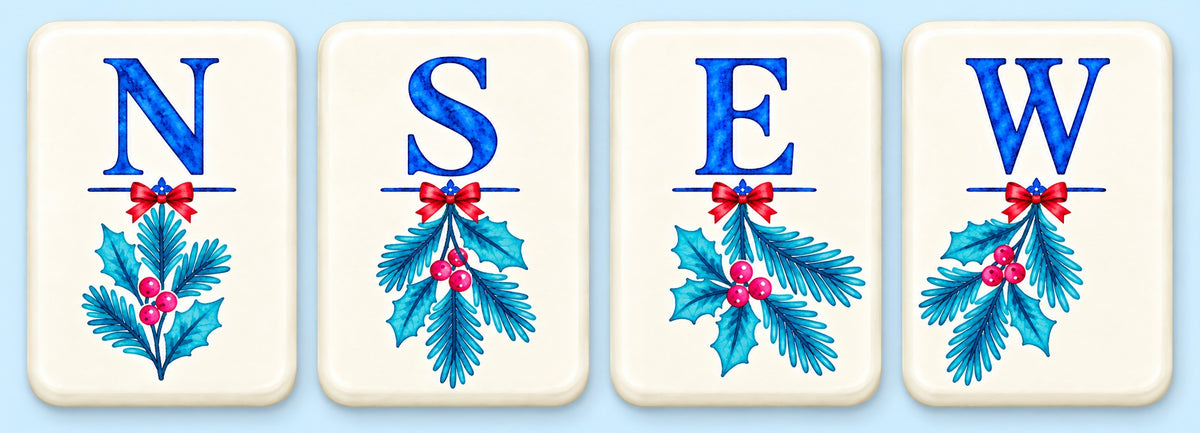 Four Alpine Escape mahjong wind tiles labeled North, South, East, and West, each decorated with blue winter foliage, red berries, and a red bow.